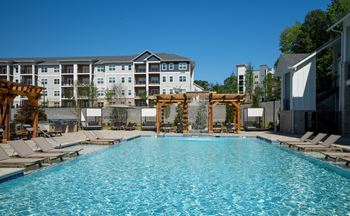 A large swimming pool with lounge chairs and a wooden pergola.